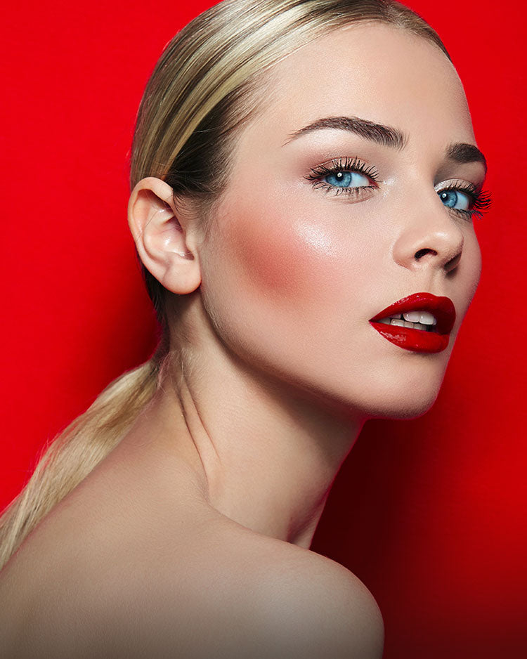 Beautiful blonde female model with blushed cheeks and red lips against a red background.
