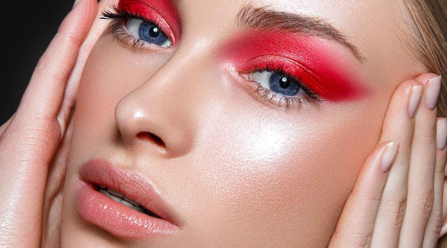 Model with red eyeshadow, glowing makeup and soft nude lip colour