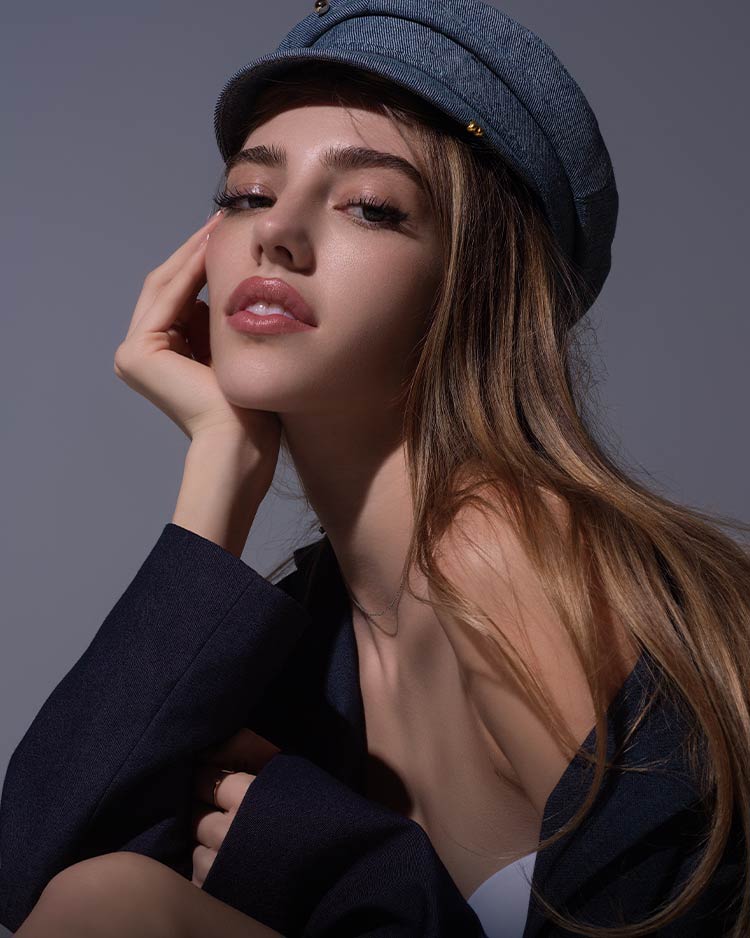 Model wearing a denim flat cap hat with soft glowing makeup and false eyelashes