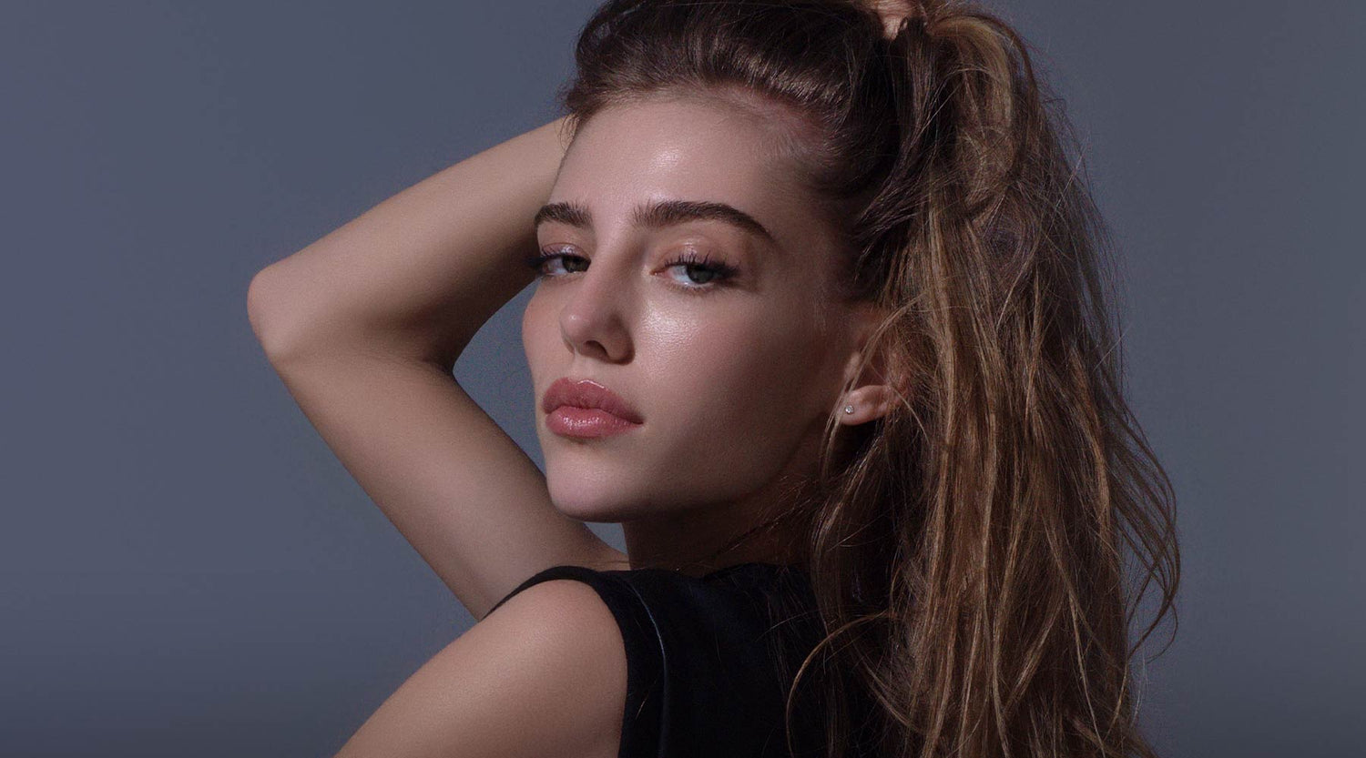Model with soft makeup and long eyelashes against a dark blue background.