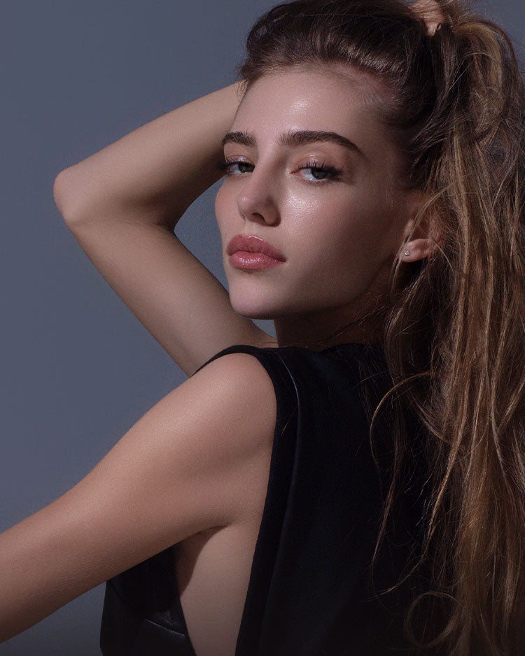 Model with soft makeup and long eyelashes against a dark blue background.