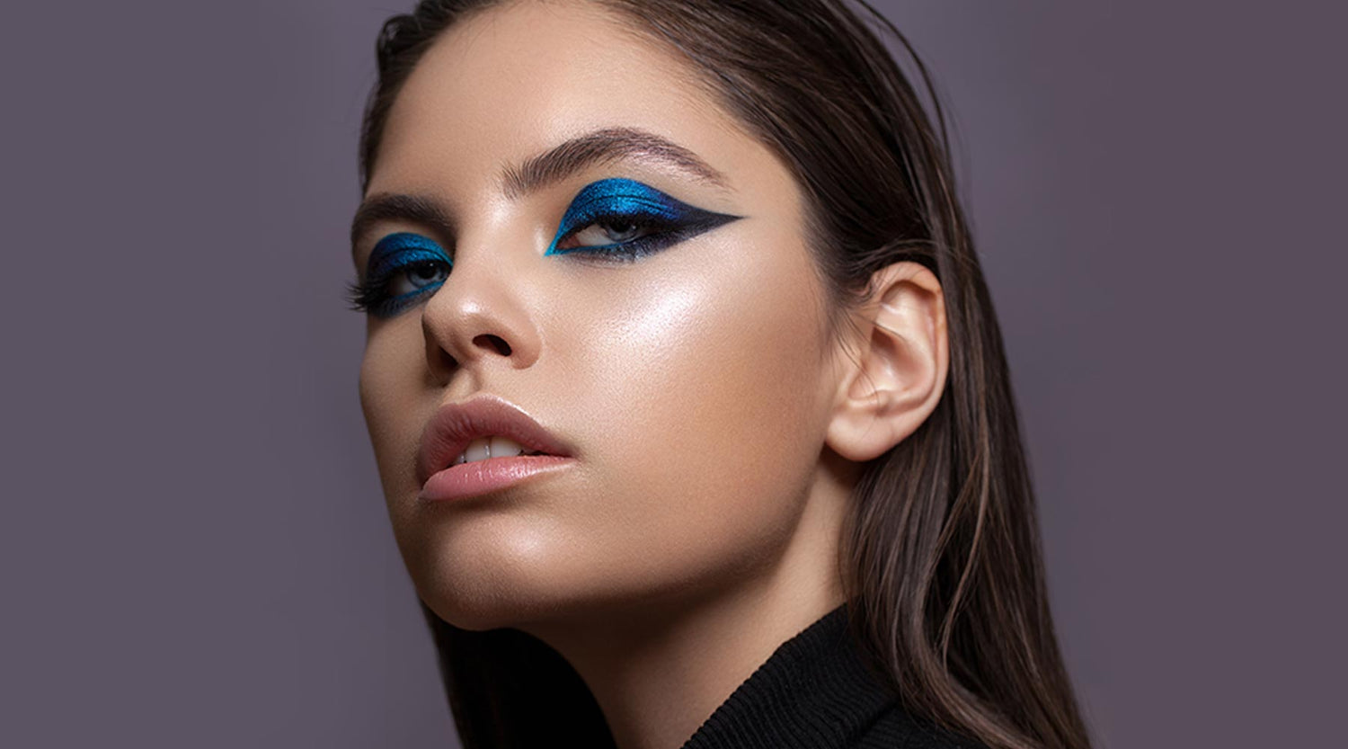 Pretty female model with vibrant blue  eyeshadow, a glowing complexion and soft nude lipstick
