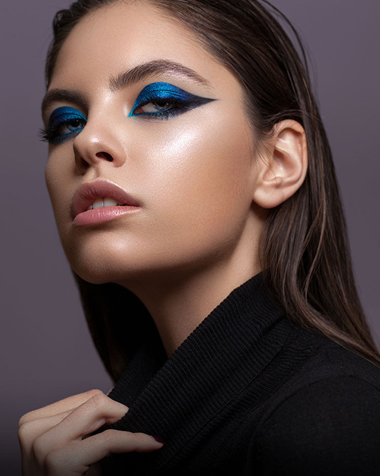 Pretty female model with vibrant blue  eyeshadow, a glowing complexion and soft nude lipstick