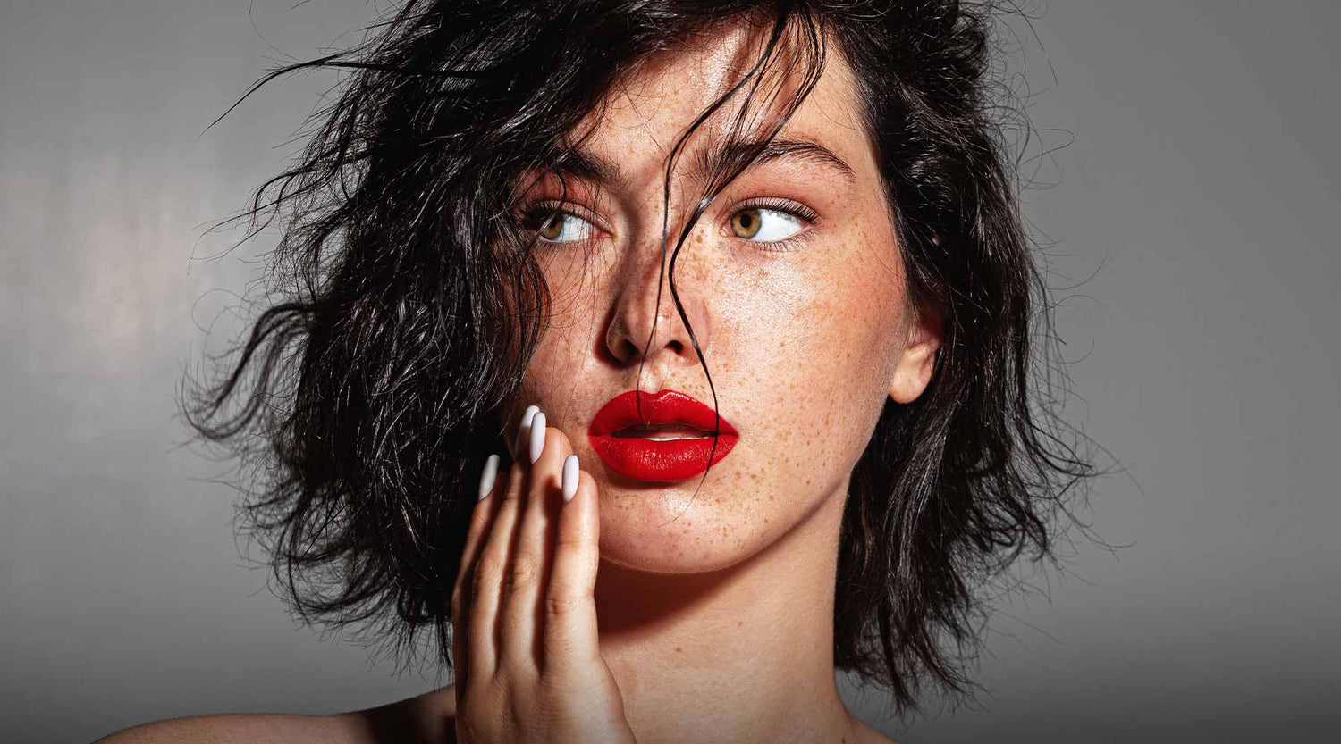 Black haired female model with freckled skin, nude makeup and bold red lips.