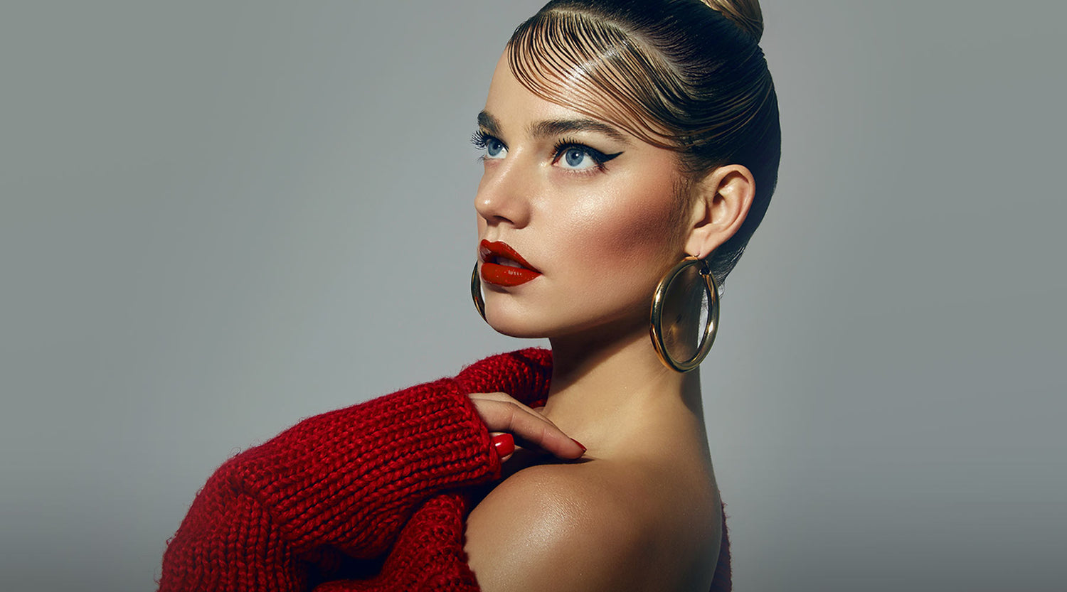 Beautiful female model with bronzed glam makeup, winged eyeliner, red lipstick with sleek styled hair and wearing red jumper.