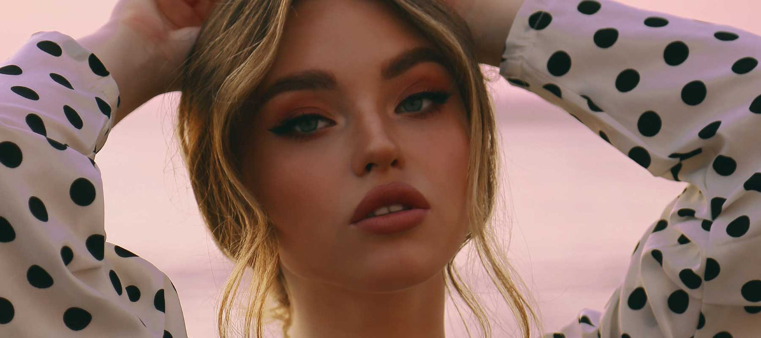 Beautiful model with brown eyeshadow, winged eyeliner and brown lipstick wearing a polka dot blouse