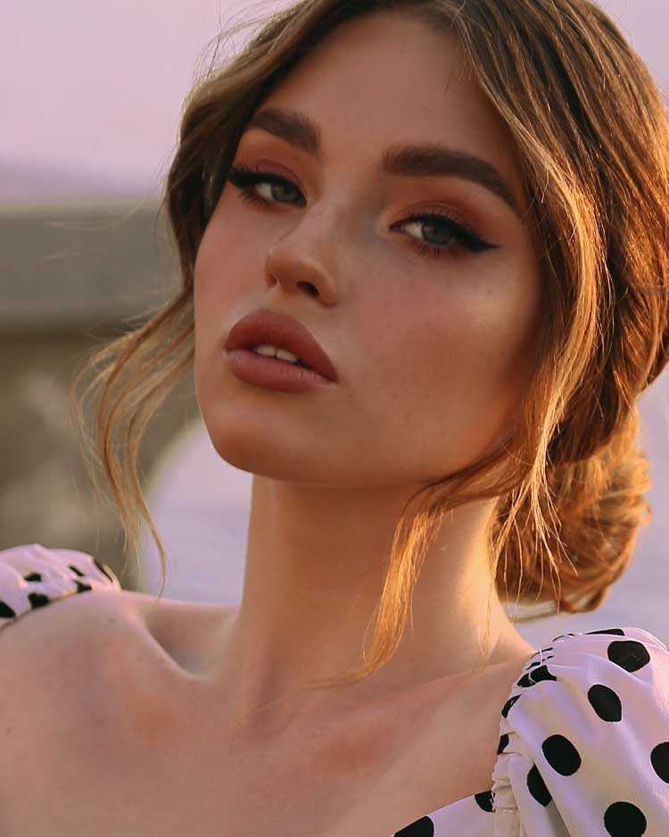 Beautiful model with brown eyeshadow, winged eyeliner and brown lipstick wearing a polka dot blouse